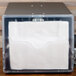 A Vollrath countertop napkin dispenser with a clear faceplate holding white napkins.