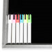 A white rectangular black marker board with a black frame on a counter with four colored markers.