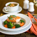 A Tuxton bright white china bowl filled with soup on a table with a plate of salmon and vegetables and a glass of wine.