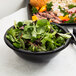 A bowl of salad with green leaves in a black Fineline Super Bowl.