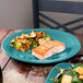 A piece of salmon and vegetables on a Fiesta® turquoise chop plate on a table.