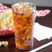 A Cambro clear plastic tumbler filled with ice tea on a table with a bowl of popcorn.