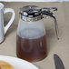 A Tablecraft syrup dispenser with a white handle on a table with pancakes.