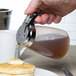A person using a Tablecraft syrup dispenser to pour syrup on a plate of pancakes.