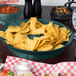 A table with a bowl of chips and salsa served in a black HS Inc. round deli server.
