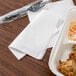 A white 1/4 fold luncheon napkin with take out food on a table.