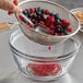 A hand holding a Tablecraft medium tin mesh strainer with berries in a bowl.