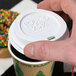 A hand using a white Eco-Products recycled content hot cup lid on a coffee cup.
