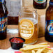A Libbey can glass of beer on a table with fries and ketchup.
