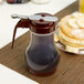 A Tablecraft polypropylene syrup dispenser with a brown lid on a table.