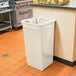 A beige Continental Swingline 32 gallon square trash can with a plastic bag in it sits in a kitchen.