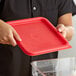 A person holding a red square container lid.