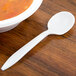 A white plastic spoon next to a bowl of soup.