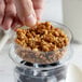 A hand holding a spoon of granola over a small plastic dish filled with cereal.