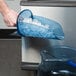 A person using a San Jamar Saf-T-Scoop to add ice to a blue container.