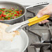 A close-up of a Vollrath stainless steel scalloped tong with a yellow Kool Touch handle.
