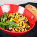 A red slanted melamine bowl filled with food next to a loaf of bread.