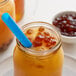 A glass jar of orange liquid with black sugar crystals with a blue spoon in it.