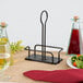A black metal Tablecraft Marbella rack with oil and vinegar on a table with a plate of salad and a glass of red liquid.