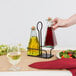 A Tablecraft metal rack holding a glass bottle of yellow liquid and a glass bottle of liquid on a table with a plate of salad.