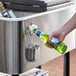 A person pouring beer into a green bottle using a Choice stainless steel beverage cooler cart.