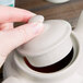 A person's hand holding a white Hall China teapot lid.