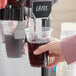A person pouring Narvon grape beverage from a dispenser into a plastic cup.