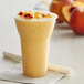 A 15 oz. clear plastic parfait cup filled with a yellow smoothie and topped with peach slices.