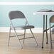 A Lancaster Table & Seating grey fabric folding chair with a padded seat next to a table.
