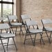 A group of Lancaster Table & Seating grey fabric folding chairs with white cushions in a room.