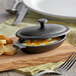 A black cast iron oval casserole dish with a lid on a wooden board with bread slices.