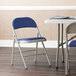A blue Lancaster Table & Seating folding chair with a padded seat next to a table.
