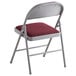 A Lancaster Table & Seating folding chair with a red cushion.