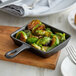 A Vollrath mini cast iron skillet with roasted brussels sprouts on a wooden board.