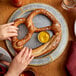 A person's hands holding a J & J Snack Foods Bavarian soft pretzel on a plate with mustard.