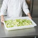 A chef holding a white Rubbermaid food storage box filled with lettuce.