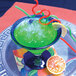 A green drink with straws and a slice of orange on a table.