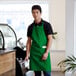A man wearing a Choice Kelly Green bib apron standing behind a coffee counter.