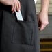 A person holding a knife in a pocket of a black restaurant apron.