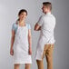 A man and woman wearing Choice white customizable bib aprons.