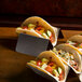 A Vollrath stainless steel taco holder with tacos on a table.