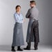 A man and woman wearing Choice grey bistro aprons standing in a professional kitchen.