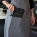 A woman wearing a Choice gray standard bistro apron with a book and pen in the pocket.