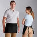 A man and woman standing next to each other wearing black Choice aprons with standard waist ties.