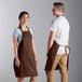 A man and woman wearing Choice brown bib aprons.