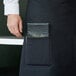 A person's hand holding a black Choice bistro apron with black pockets.