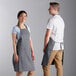 A man and woman wearing Choice grey bib aprons with 2 pockets.