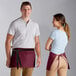 A man and woman wearing burgundy Choice standard waist aprons with 3 pockets.