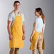 A man and woman standing next to each other in yellow Choice poly-cotton bib aprons.