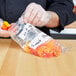 A person in gloves holding a plastic bag of peppers.